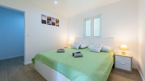 Un dormitorio con colcha verde, dos lámparas de noche, una mesita de noche y una ventana con persianas.