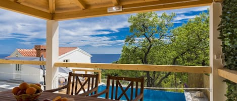 A wooden deck with a table set for breakfast, overlooking a swimming pool and a view of the sea.