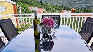 Een tafel met een fles en glazen, een roze bloemstuk en uitzicht op een berg en gebouwen.