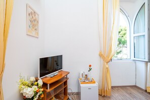 Una stanza con una TV a schermo piatto su un supporto in legno, un piccolo elettrodomestico bianco e una finestra con tende.
