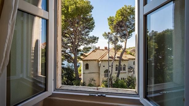 Ein Fenster mit Blick auf ein Gebäude mit einem Ziegeldach und Bäume im Vordergrund.