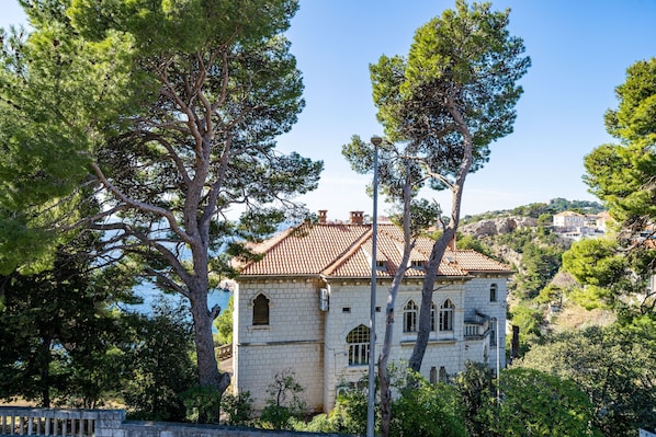 A historic stone building with a tiled roof, surrounded by trees and overlooking a hillside.