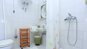 Un bagno con il water, un lavandino, una doccia e uno scaffale con asciugamani.