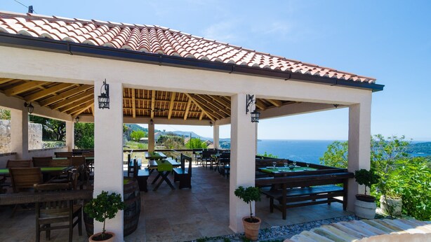 Un'area relax esterna coperta, con tavoli, sedie, piante in vaso e vista sul mare.