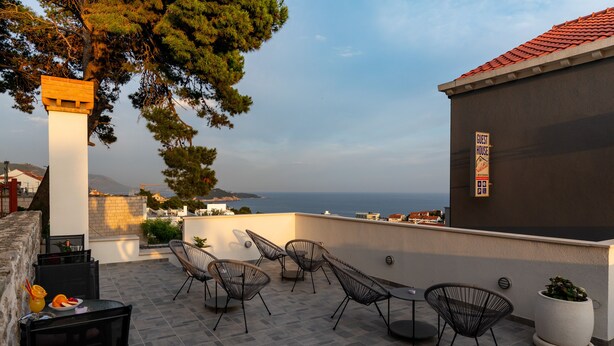 A terrace with outdoor seating, a view of the sea, and a building with a sign indicating a guest house. - Guest House Nikolina - Double Room(2) (Dubrovnik)