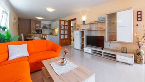 A modern living room with a bright orange sofa, a wooden coffee table, a flat-screen TV, and a kitchen area in the background. - Holiday Home Diana - Comfort Two Bedroom Apartment with Terrace and Sea View (Vela Luka)