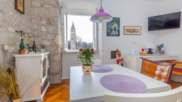 A dining area with a white table, purple placemats, a potted plant, and a stone wall. - Old City Center Suite - One Bedroom Suite (Split)