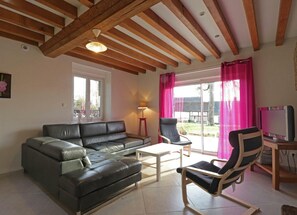Una sala de estar con un sofá de cuero negro, una mesa de centro de madera, dos sillones, un televisor y una ventana con cortinas rosadas.
