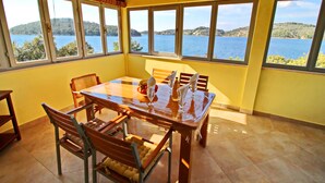 A dining area with a table set for four, large windows with a view of a lake and hills, and a yellow wall. - Holiday Home Katica - One Bedroom Holiday Home with Terrace and Sea View (Vela Luka)