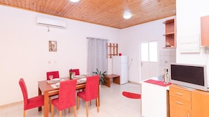 A dining area with a wooden table and red chairs, a small refrigerator, and a TV on a wooden cabinet. - Apartments Grga - Studio Apartment with Balcony and City View (Dubrovnik)