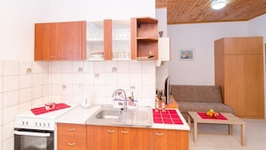 A compact kitchen with wooden cabinets, a white countertop, and a built-in oven. - Apartments Grga - Studio Apartment with Balcony and City View (Dubrovnik)