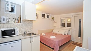 A compact bedroom with a bed, bedside table, and a window. Adjacent to the bedroom is a kitchenette with a microwave, kettle, and sink. - Nika Family Apartments - Basic Studio Apartment with External Terrace and Sea View (A5) (Dubrovnik)
