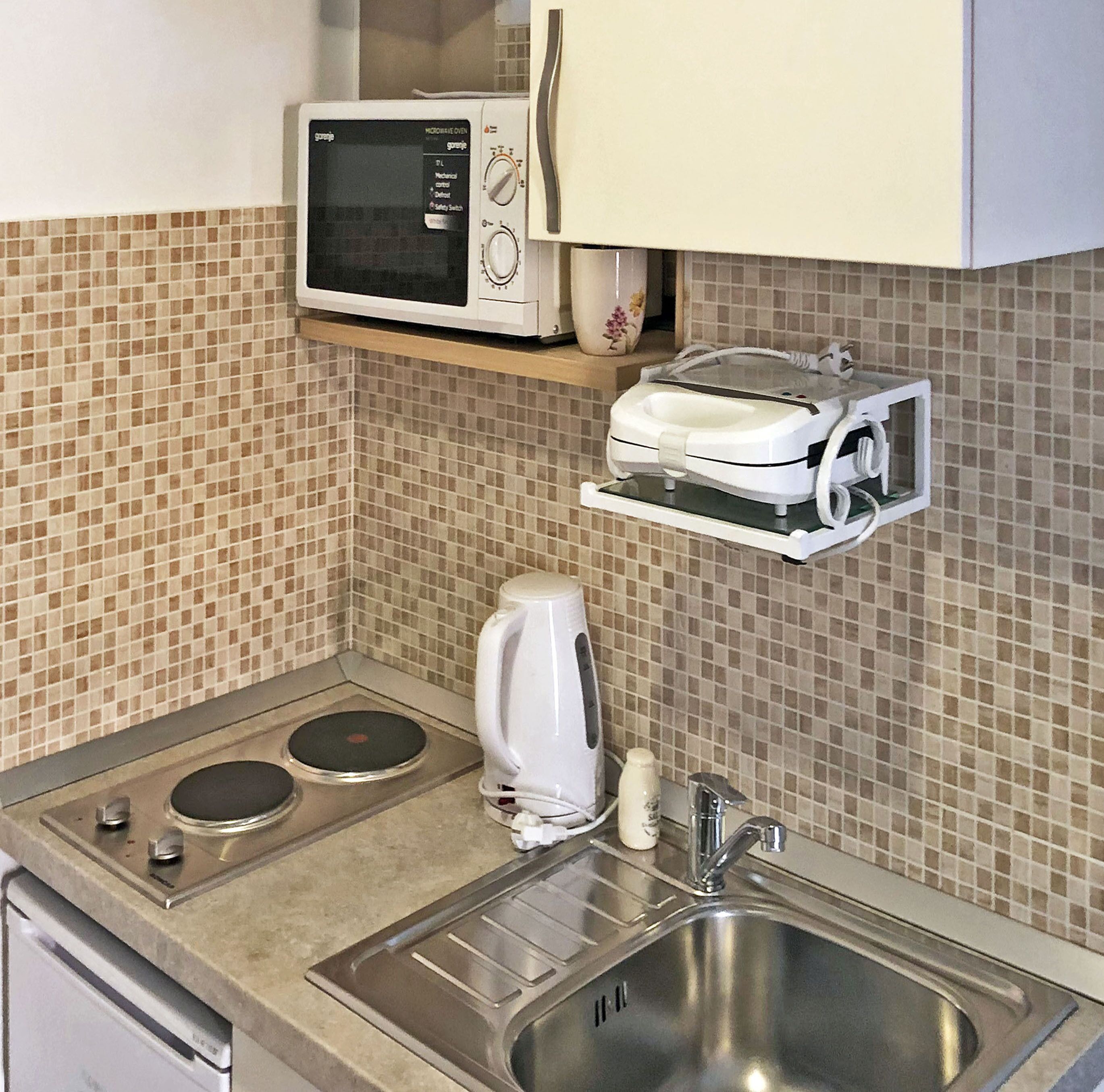 A compact kitchenette with a microwave, toaster, kettle, and a stainless steel sink.