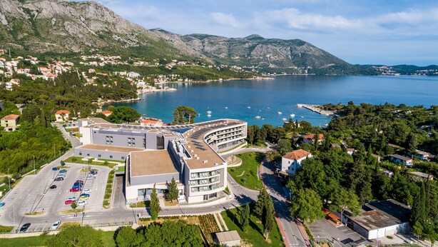 An aerial view of a coastal town with a modern building featuring multiple floors and a parking lot. - Apartments Mali Paradiso - Studio Apartment with Pool View (Mlini)