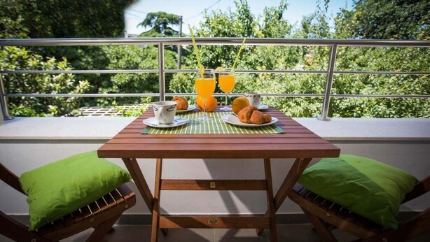 A wooden table with a green mat, two green cushioned chairs, and a breakfast setting with croissants, orange juice, and a cup.
