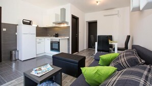 A compact living space with a kitchenette, a sofa with green and plaid cushions, a small table with a magazine, and a chair.