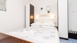A modern hotel room with a large bed, a bedside table with towels, a mirror, and a wardrobe.