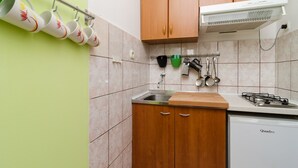 A kitchen with wooden cabinets, a gas stove, a dishwasher, and a hanging rack with cups.