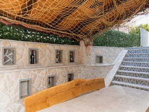 Una pared de piedra con espacio para almacenamiento de vino, un banco de madera y una estructura de red en el techo.