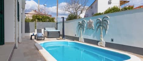 Una piscina con un borde de baldosas, un jacuzzi y una pared decorada con motivos de palmeras.