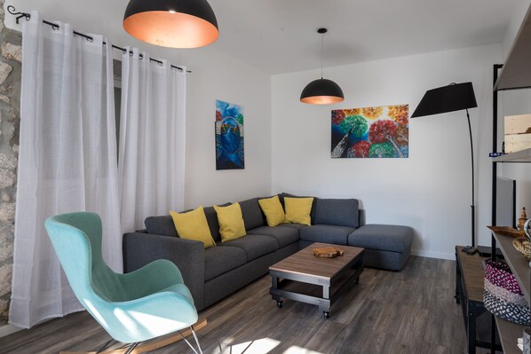 Ein modernes Wohnzimmer mit einer Eckcouch, einem türkisfarbenen Sessel, einem Couchtisch und Kunstwerken an den Wänden.