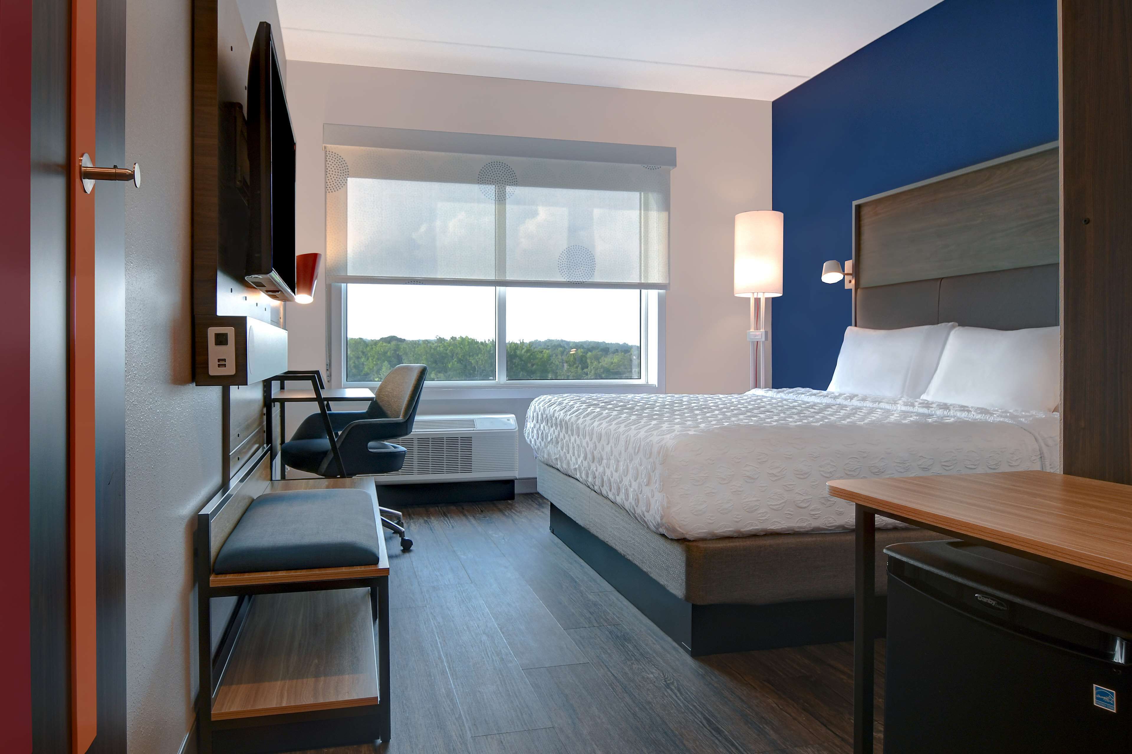Habitación de hotel con cama, escritorio, silla, televisor y ventana.