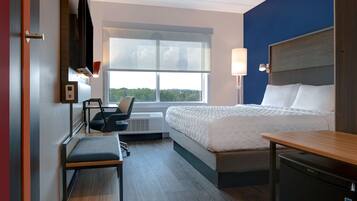 Habitación de hotel con cama, escritorio, silla, televisor y ventana.