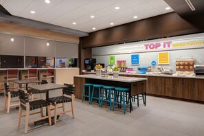 Enjoy a casual breakfast at the TOP IT BREAKFAST area, featuring a central island with stools and a selection of pastries and beverages.