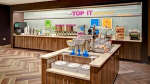 Un área de desayuno con una barra que exhibe diversos alimentos y un letrero que dice "TOP IT BREAKFAST".