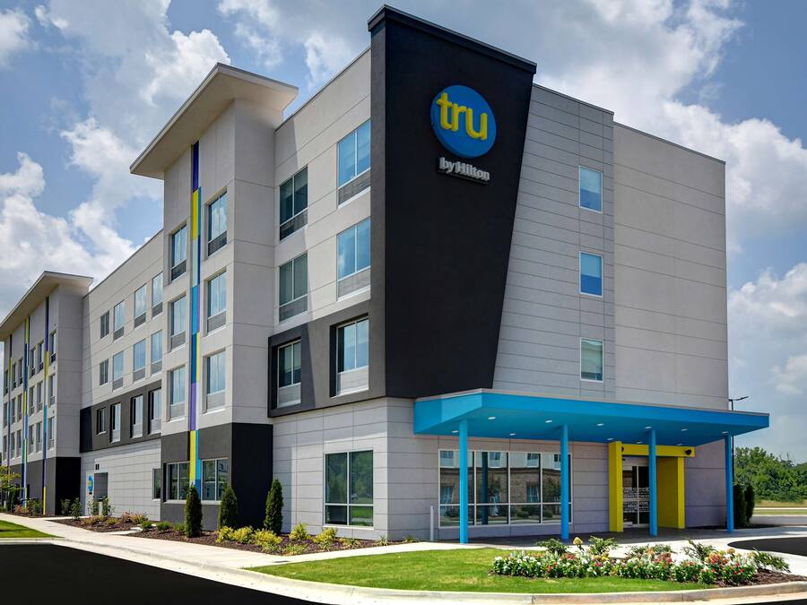 Un moderno edificio de hotel con un llamativo letrero 'tru by Hilton', varios pisos y una zona de entrada cubierta.