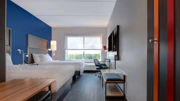 A modern hotel room with two beds, a desk, a chair, a TV, and a large window.
