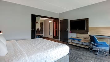 A modern hotel room with a large bed, a desk with a chair, a flat-screen TV, and a wooden headboard.