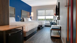 Habitación de hotel con dos camas, un escritorio, una silla, un televisor y una ventana con vistas.