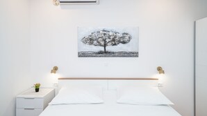 Un dormitorio con cama, mesitas de noche, aire acondicionado instalado en la pared y un cuadro de un árbol.