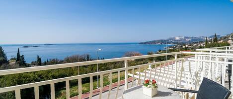A balcony with a view of the sea, a round table with chairs, and a potted plant.