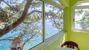A room with large windows overlooking a body of water, a stone birdhouse, and a table with a chair. - Seafront Apartments Olivera-One Bedroom Apartment with Balcony and Sea View ( Ante ) (Vela Luka)