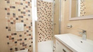 Ein Badezimmer mit Wandfliesen aus Mosaik, einer Duschkabine aus Glas, einem weißen Waschbecken und einem Spiegel.