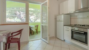 A kitchen with white cabinets, a gas stove, and a built-in oven. There is a dining area with a table and chairs, and a sliding glass door leading to an outdoor balcony.