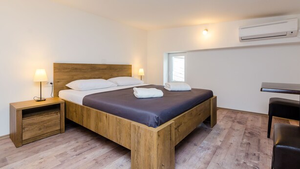 Una cama individual con estructura de madera, una mesita de noche con lámpara, un escritorio y un equipo de aire acondicionado en la pared.