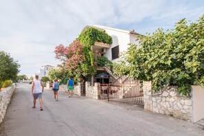 Stroll through a charming residential street lined with trees and shrubs, featuring a two-story house with a balcony surrounded by lush greenery.