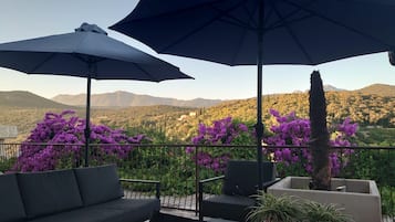 Un balcon doté d’un espace salon extérieur, comprenant un canapé et des fauteuils, ainsi que deux grands parasols pour créer de l’ombre.