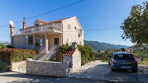 A two-story house with a balcony, a car parked in front, and a mountainous landscape in the background.