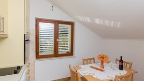 A dining area with a table set for two, a window with blinds, and a bottle of wine on the table.