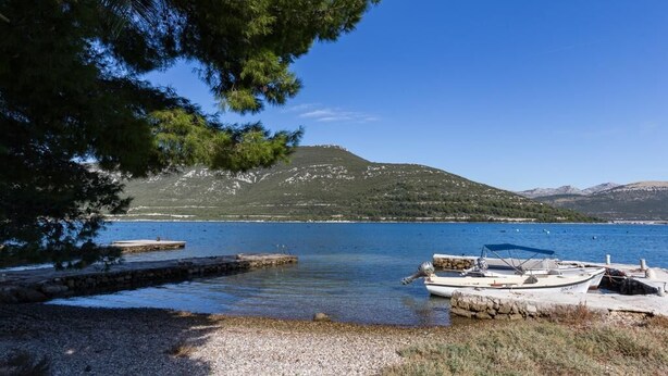 A calm lake with boats docked at a pier, surrounded by mountains and trees.