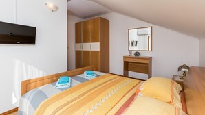 A bedroom with a bed, a wardrobe, a bedside table, a mirror, and a TV mounted on the wall.