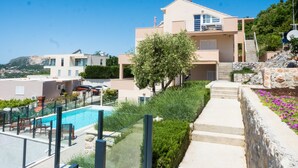 Un edificio moderno de dos pisos con piscina, un muro de contención de piedra y una escalera que lleva a un balcón.