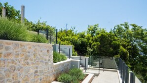 Un espacio exterior moderno con muros de piedra, barandillas metálicas y vegetación.