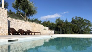 Una piscina con sillas de descanso, paredes de piedra y árboles al fondo.