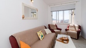 Una sala de estar con un sofá color beige, dos sillones, una mesa de centro, un ventanal con persianas y un espejo montado en la pared.