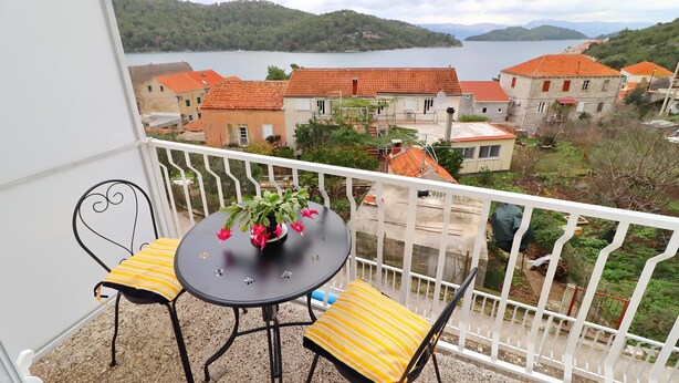 En balkon med et bord og stole, udsigt over en sø og bygninger.